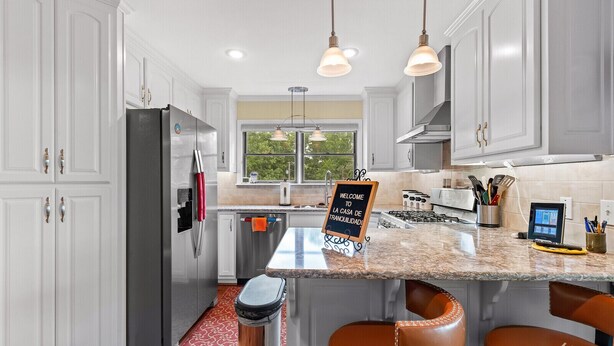 A modern kitchen with white cabinetry, stainless steel appliances, a granite countertop, and a chalkboard sign.