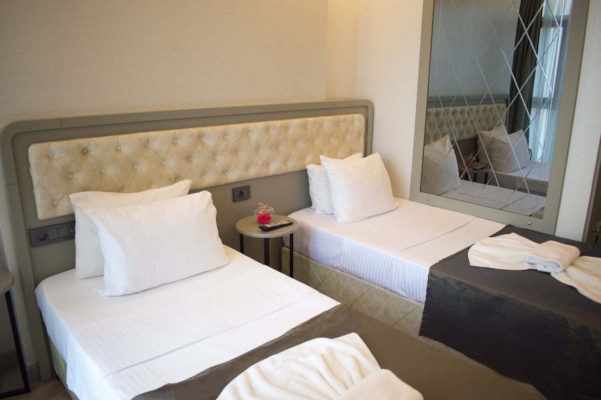 Ein Hotelzimmer mit zwei Betten, einem kleinen Tisch mit einer Fernbedienung und einem Spiegel, der den Raum reflektiert.