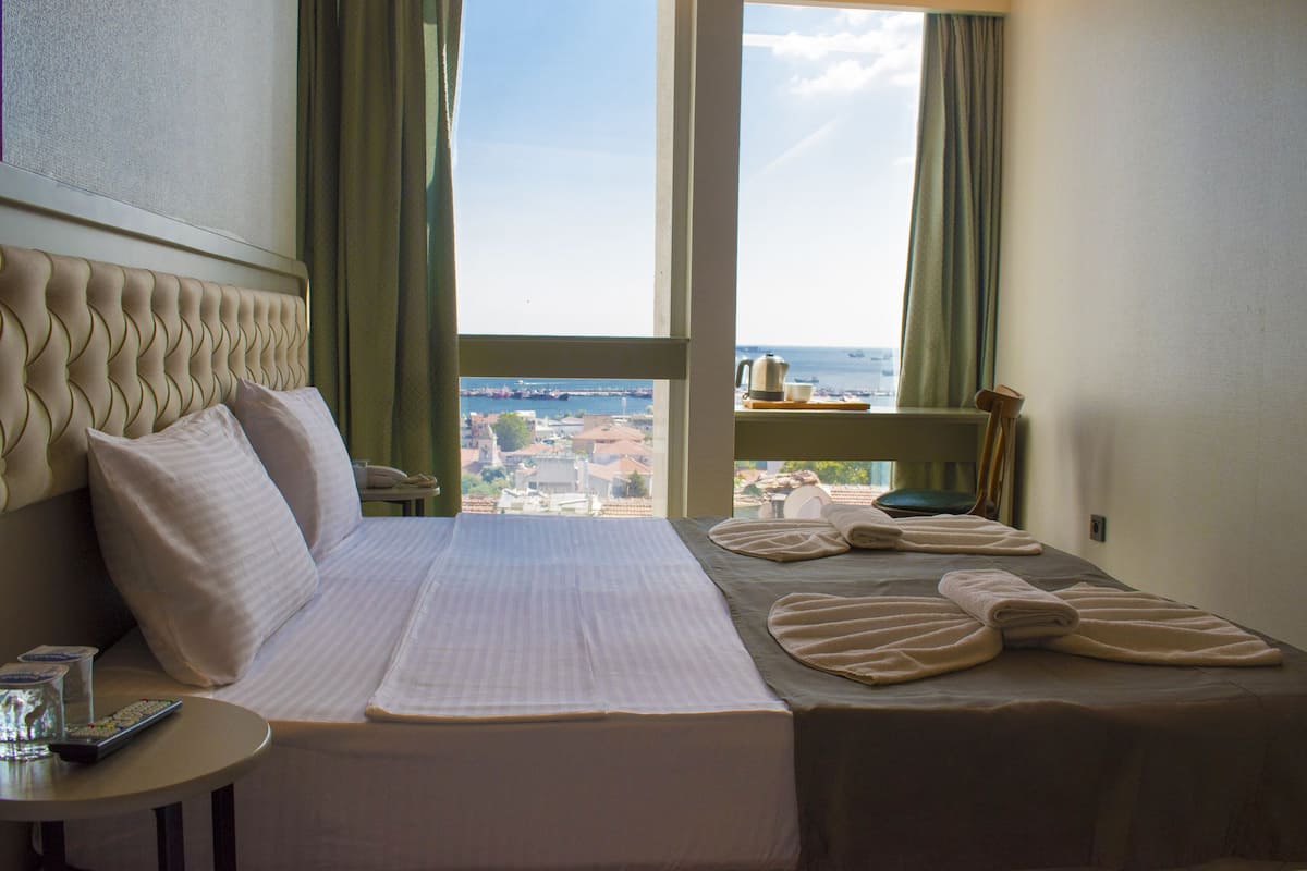 Ein Hotelzimmer mit einem großen Bett, einem Nachttisch mit Fernbedienung und Blick auf die Stadt durch das Fenster.