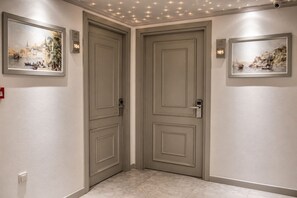 Un pasillo con dos puertas, cada una con una placa numerada, y cuadros enmarcados en las paredes.