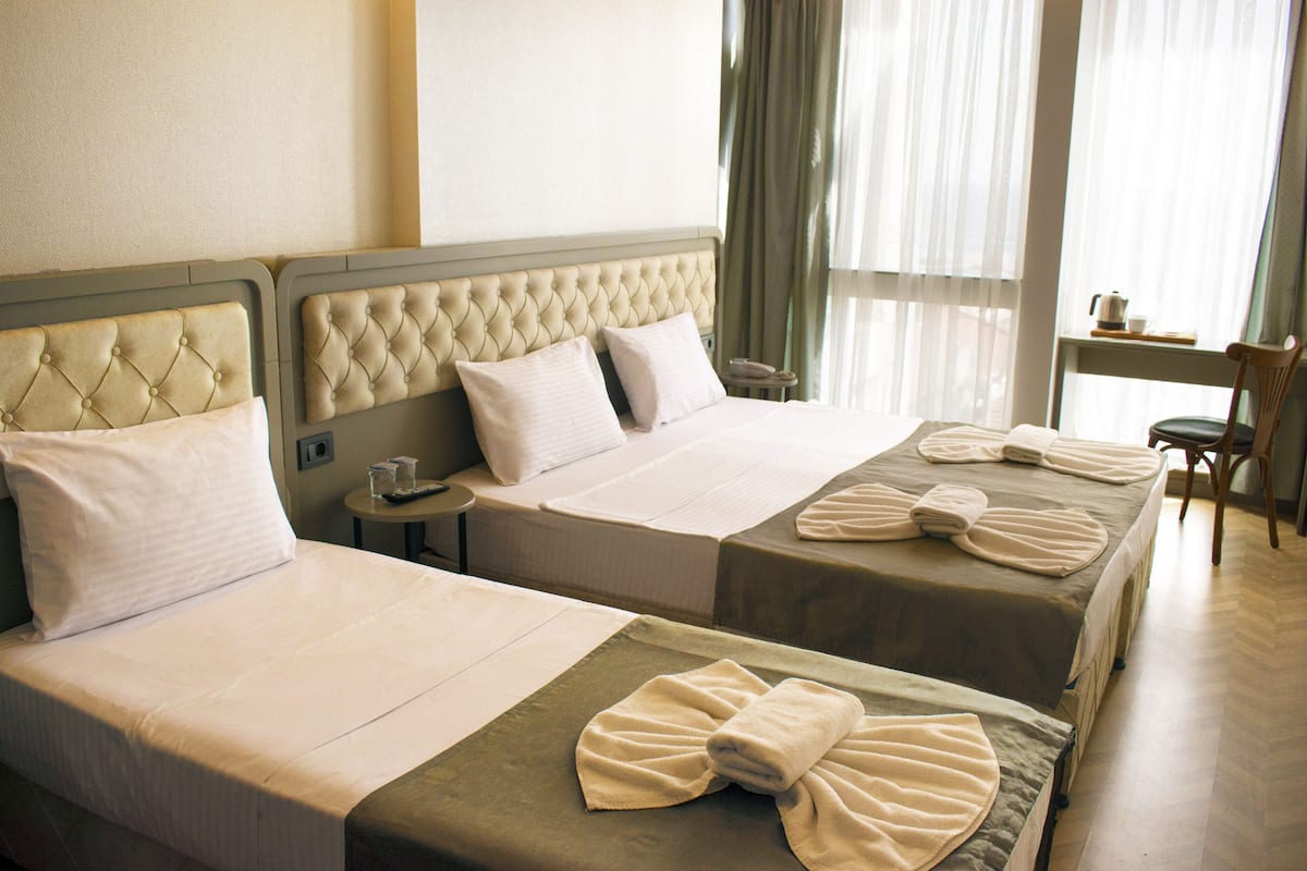Ein Hotelzimmer mit zwei Betten, jeweils mit einem gesteppten Kopfteil, weißen Leinentüchern und ordentlich gefalteten Handtüchern.