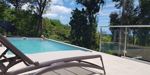 Un espace piscine offrant une vue dégagée sur la végétation environnante et doté d’une rambarde en verre.