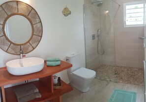 Une salle de bain avec un miroir rond, un lavabo blanc et une douche à parois de verre.