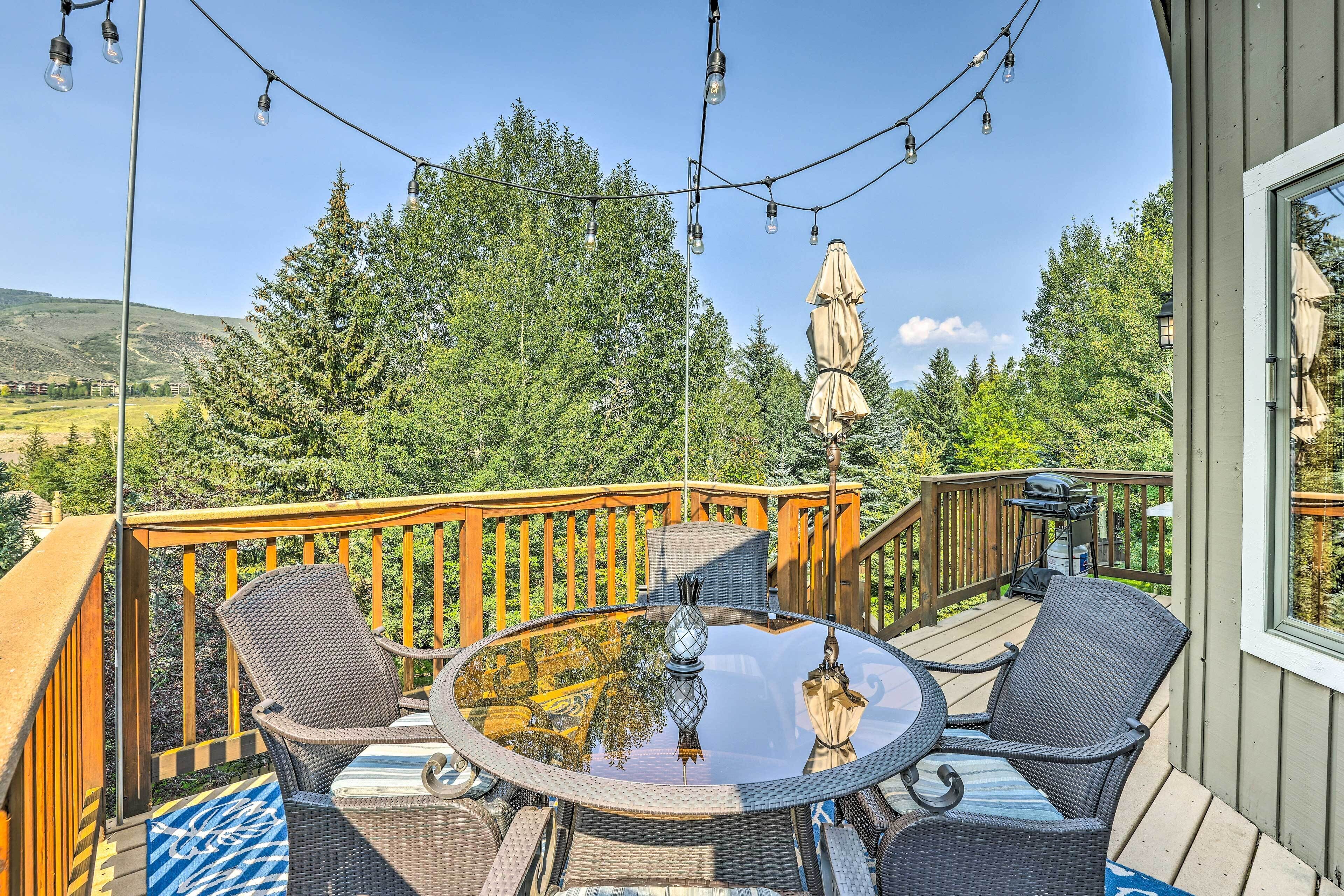Eine Terrasse mit Korbmöbeln, einem Glastisch und Lichterketten.