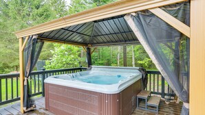 Un jacuzzi en una terraza de madera con zona cubierta y una pequeña mesa.