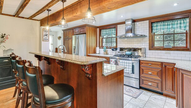 Una cocina con armarios de madera, una isla central, taburetes de bar e iluminación colgante.