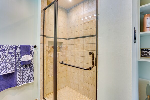 Ducha con puerta de vidrio, toallero con toallas estampadas y un cartel en la pared.