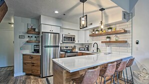 Une cuisine moderne dotée d’un îlot central, d’appareils électroménagers en acier inoxydable, de meubles de rangement en bois et de tabourets de bar.