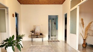 A spacious room with a wooden ceiling, patterned floor tiles, a bench, a potted plant, and a vase with dried plants.