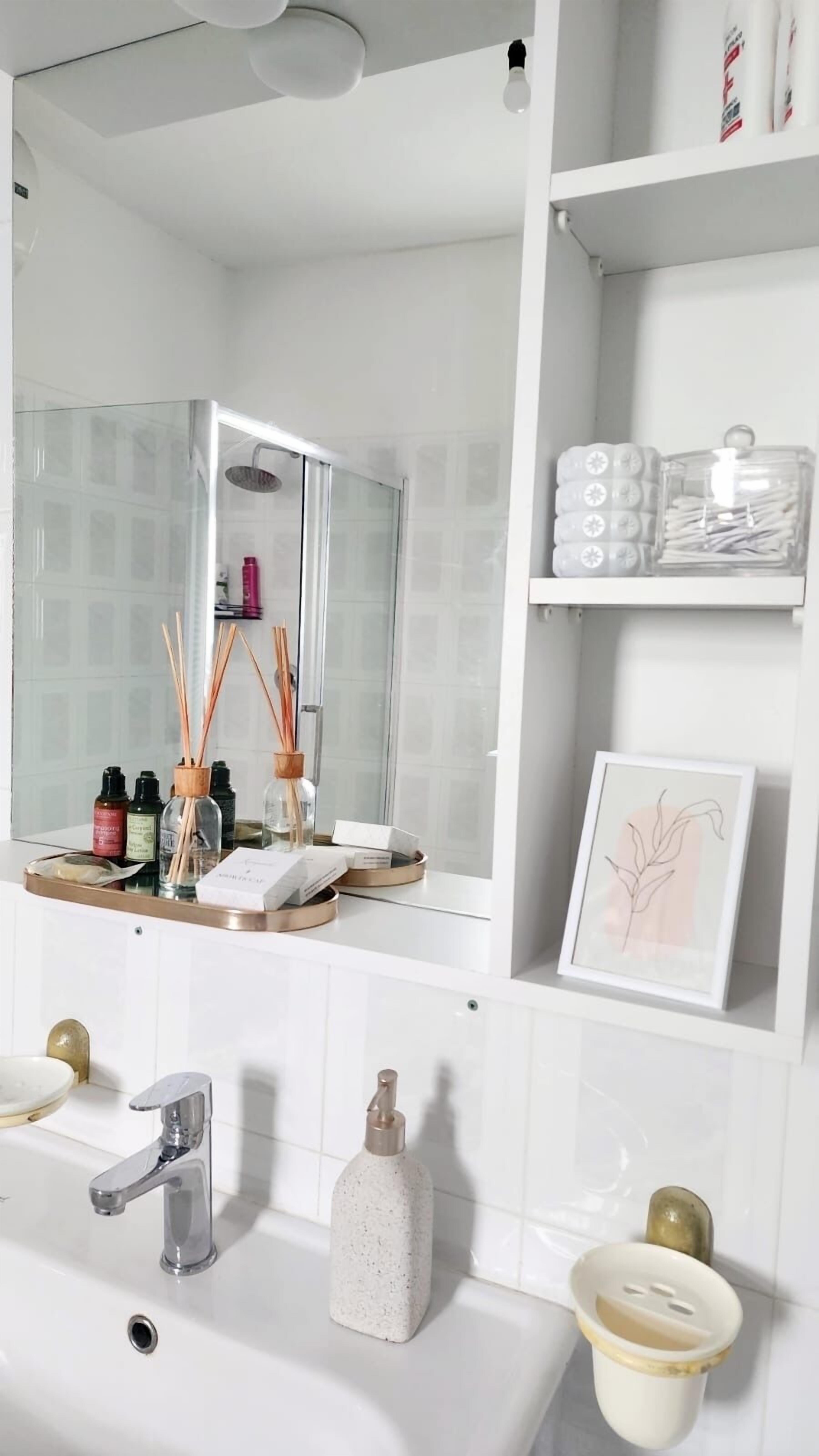 Une salle de bain moderne avec un grand miroir, des carreaux blancs, un lavabo avec un seul robinet et un espace douche.