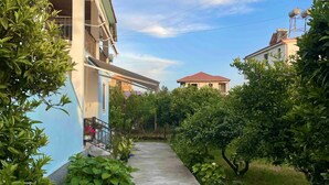 A pathway flanked by lush greenery and buildings with balconies, leading to a building with a red roof.