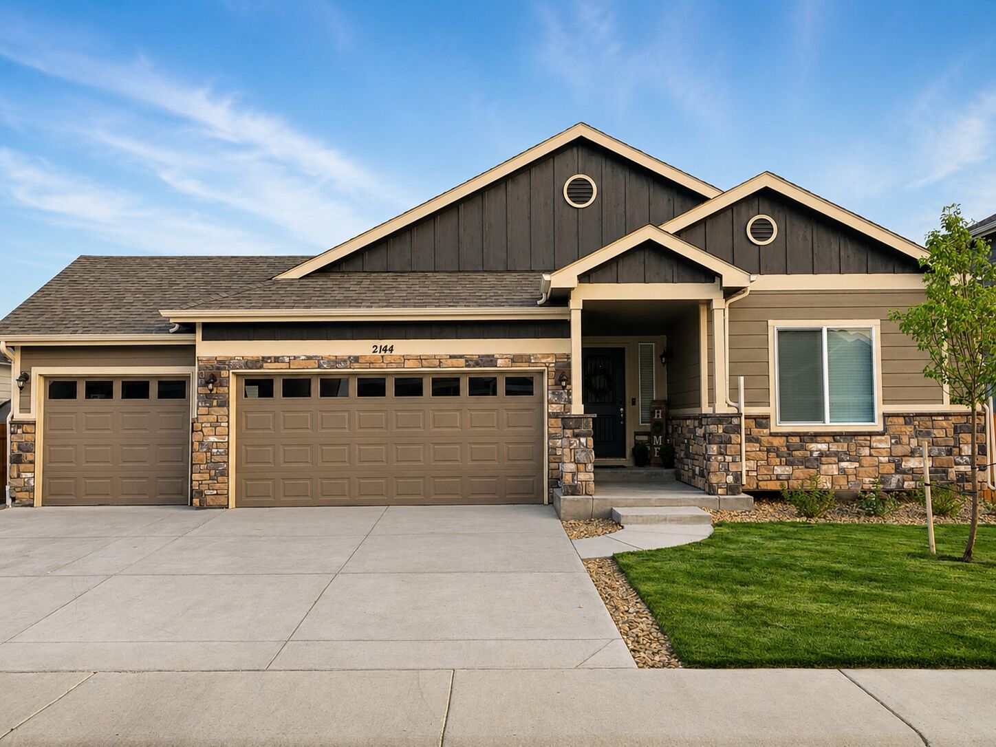 A two-story house with a garage, a stone facade, and a well-maintained lawn.
