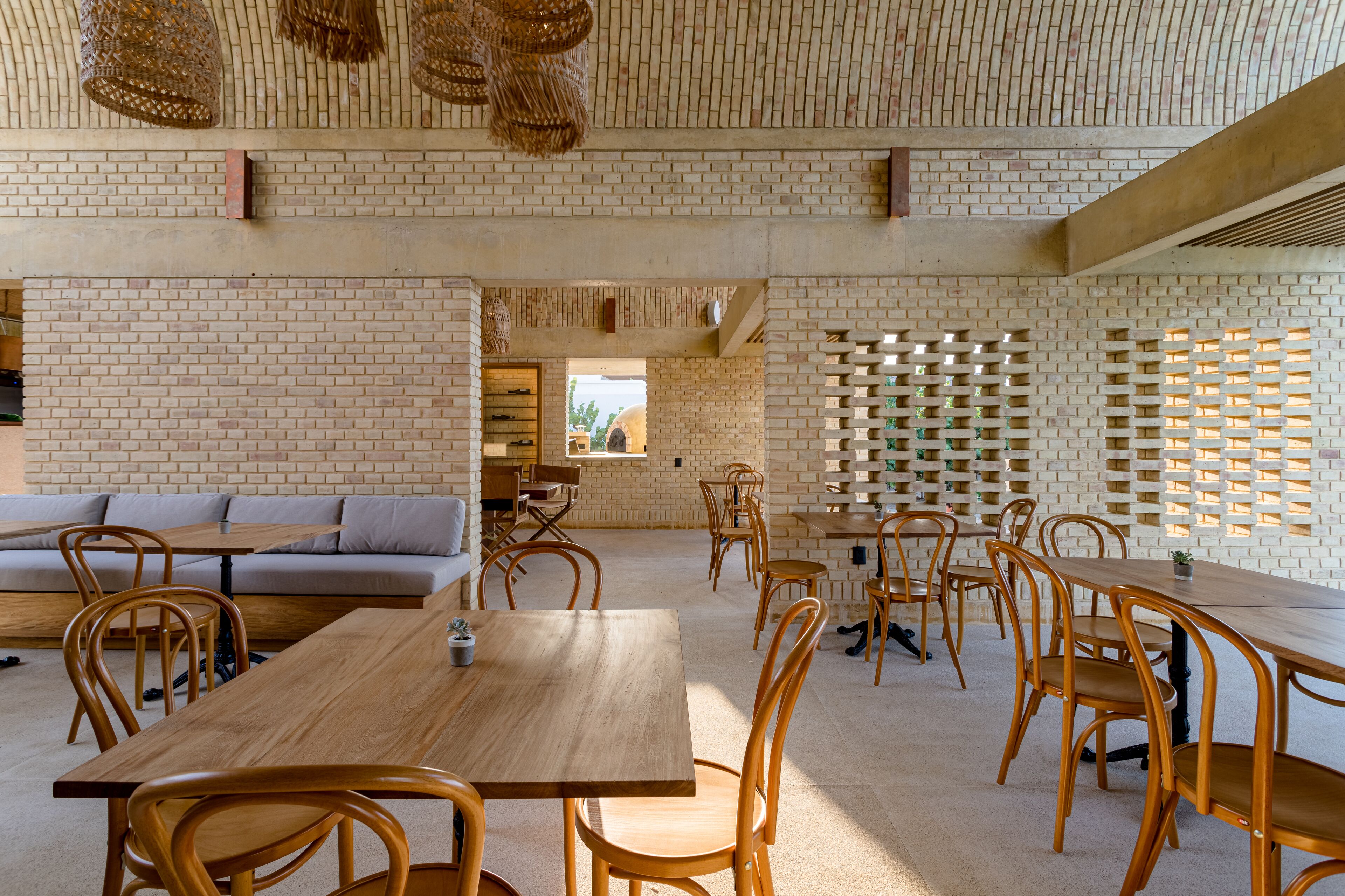 Un vaste espace dédié à la salle à manger, avec des murs en briques, des tables et des chaises en bois, et une grande fenêtre qui laisse entrer la lumière naturelle.