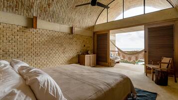 A bedroom with a large bed, a ceiling fan, and a view of the outdoors.