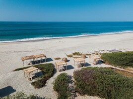 Vista aérea de una playa con estructuras de techo de paja y una vista despejada del océano.