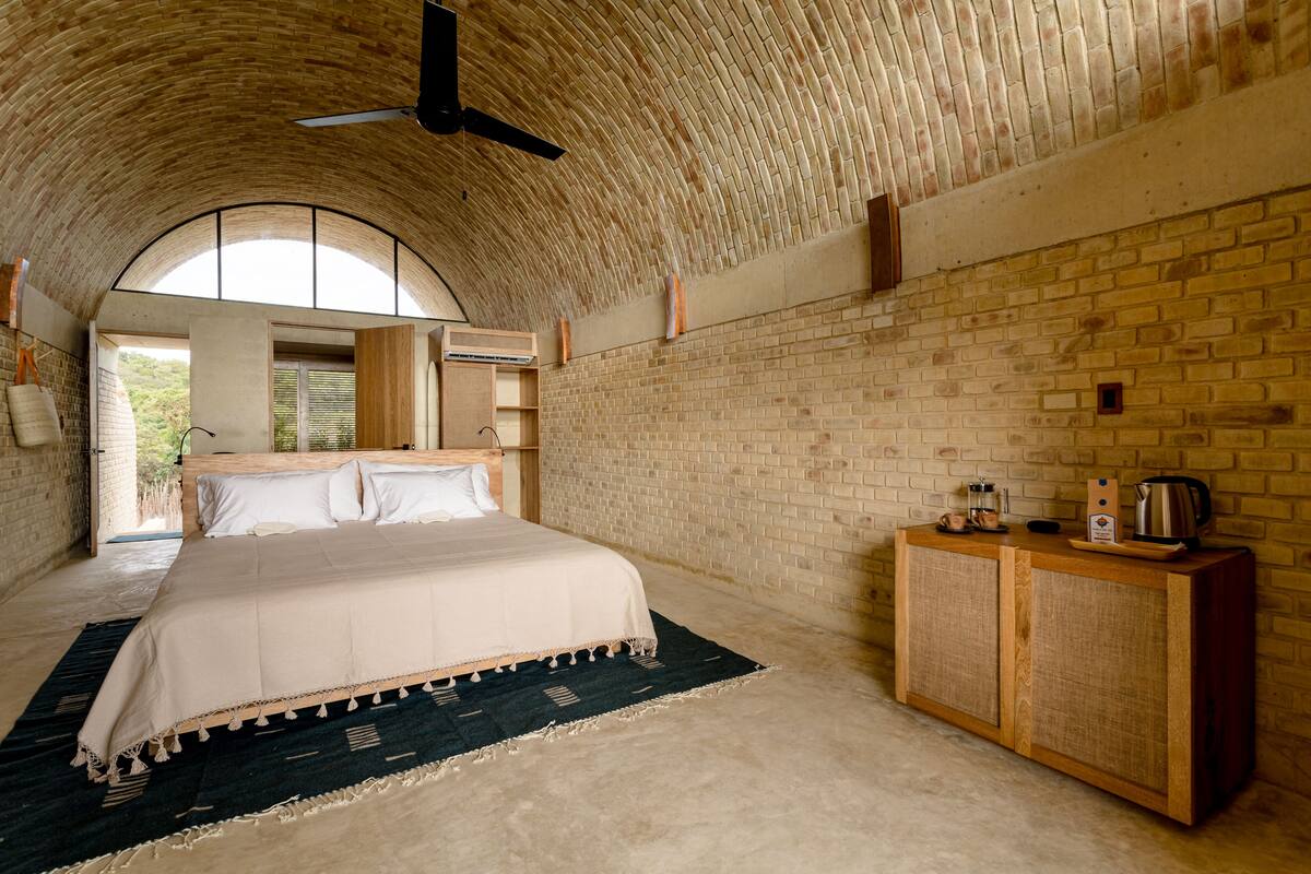 A bedroom with a large bed, a wooden cabinet, and a brick wall.