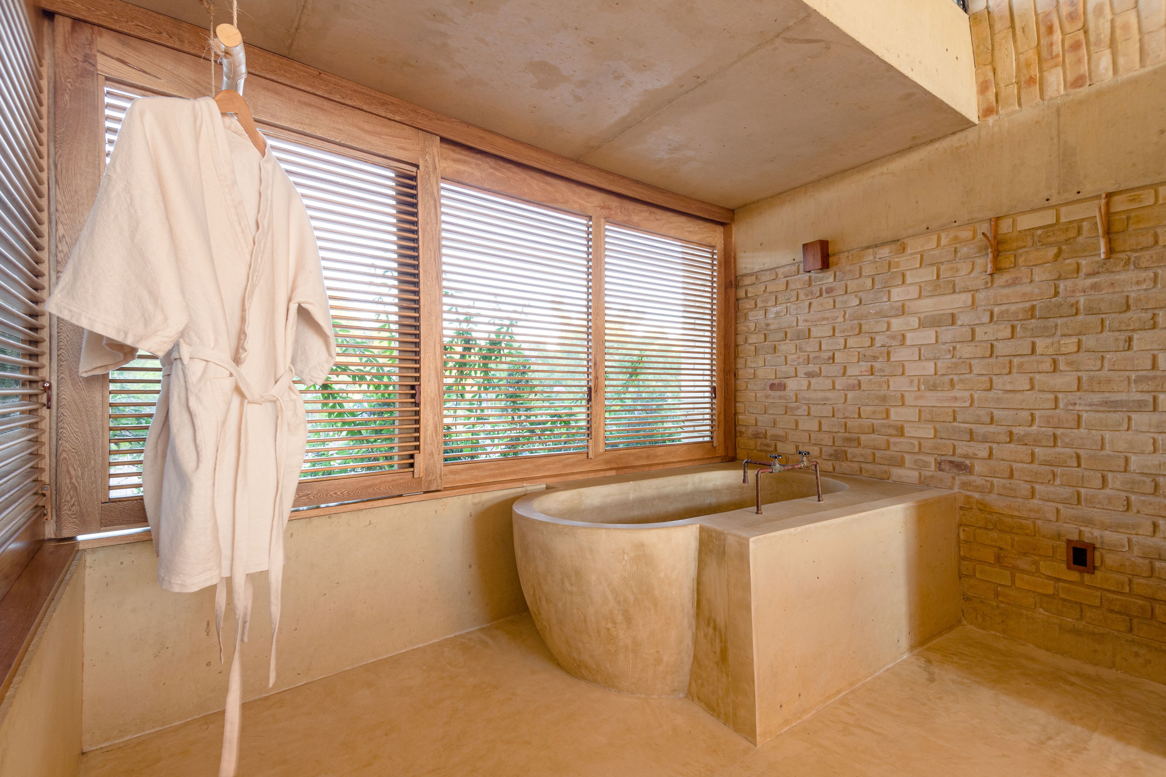 A modern bathroom with a freestanding bathtub, wooden blinds, and a hanging bathrobe.