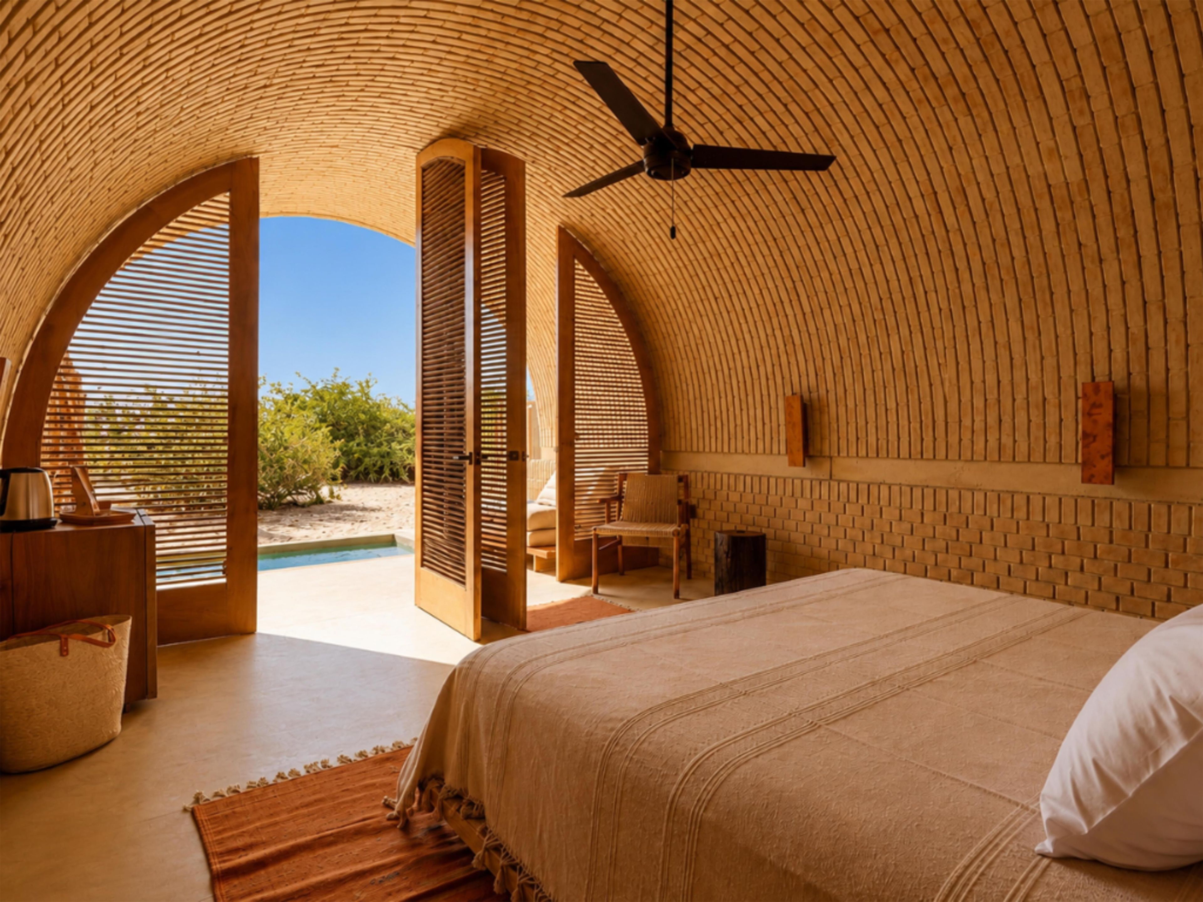 Un dormitorio con una cama grande, un ventilador de techo y vistas a una piscina y follaje exterior.