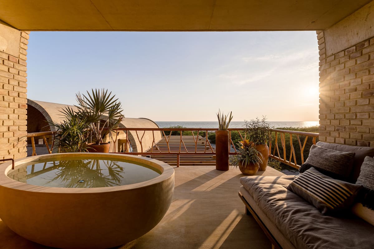 A balcony with a large hot tub, a sofa, and potted plants.