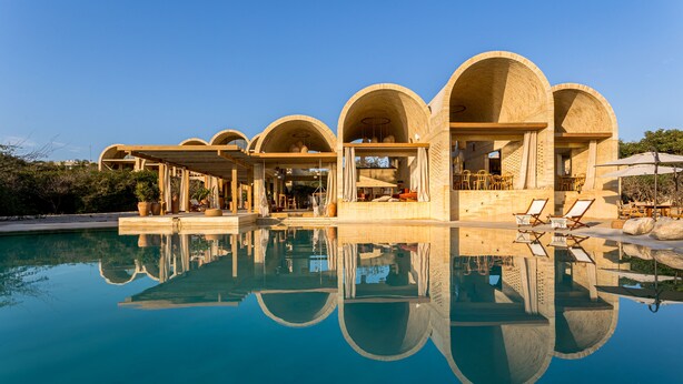A poolside area with a clear reflection, outdoor seating, and a building with arched structures.