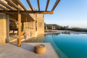 A modern pool area with a clear view of the pool, a wooden pergola, and a seating area with outdoor furniture.