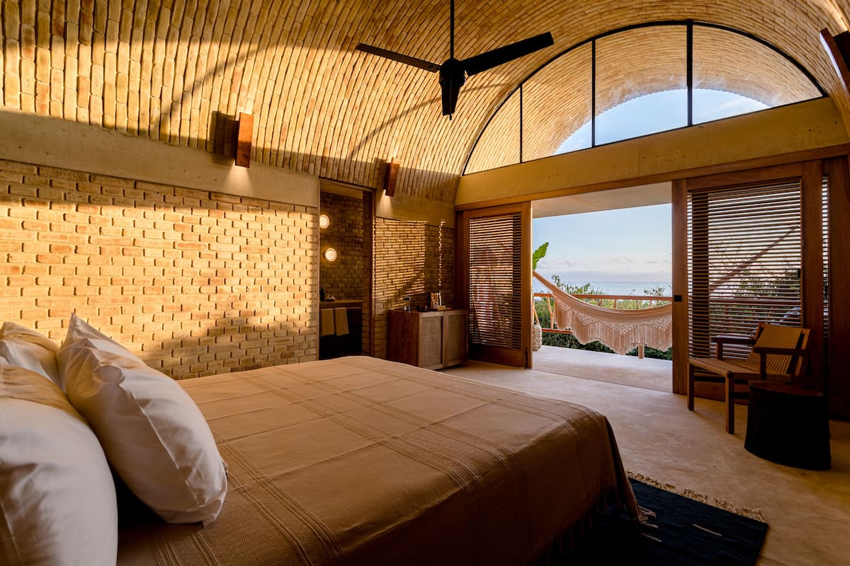 A bedroom with a large bed, a ceiling fan, and a view of the outdoors.