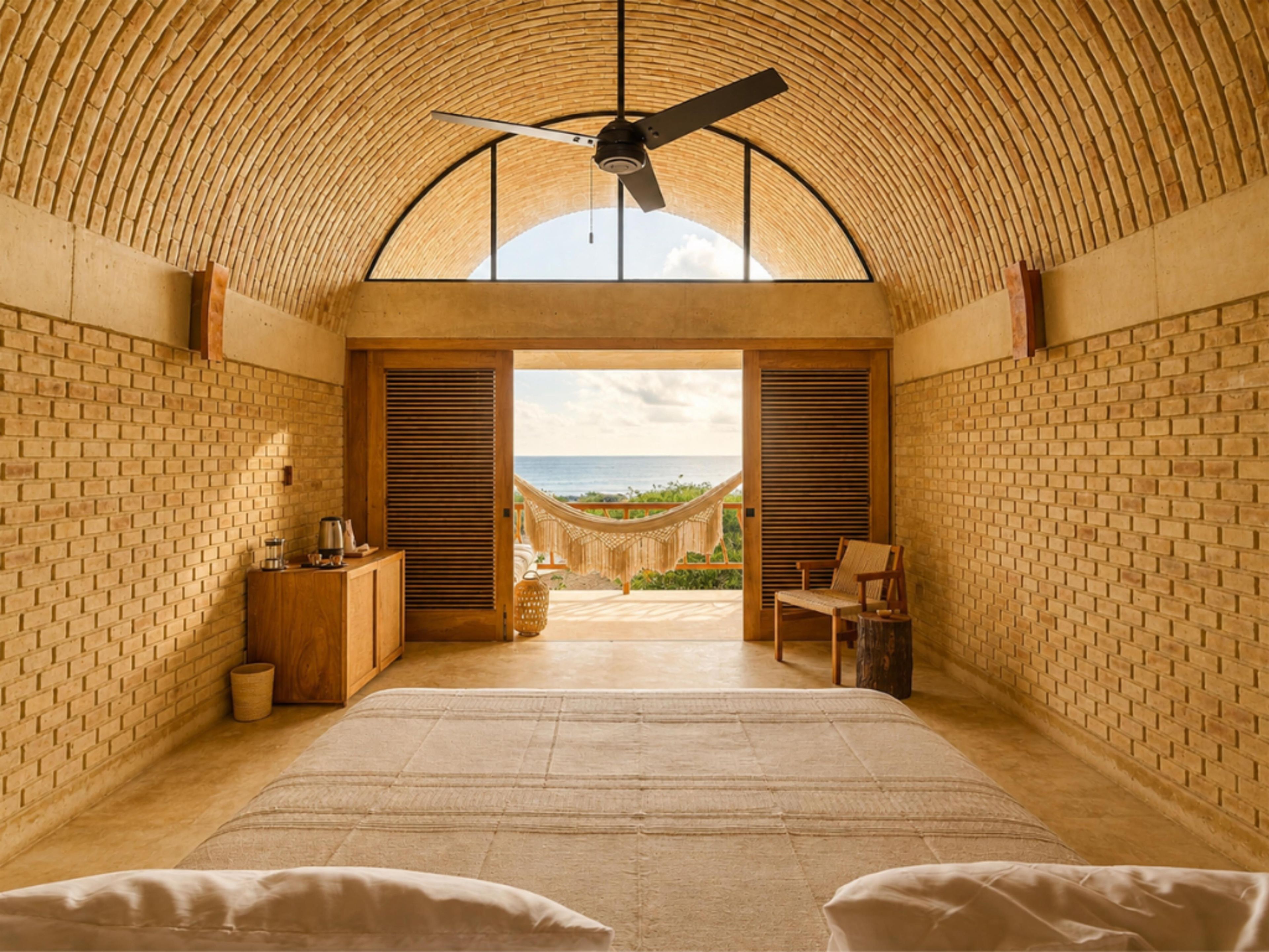 A room with a high ceiling, a bed, a wooden cabinet, and a view of the ocean through a doorway.