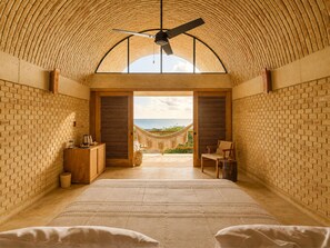 Habitación con techo alto, una cama, un armario de madera y vista al océano a través de un vano.