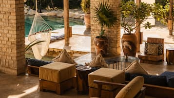 Zona junto a la piscina con mobiliario exterior, una hamaca y plantas en macetas.