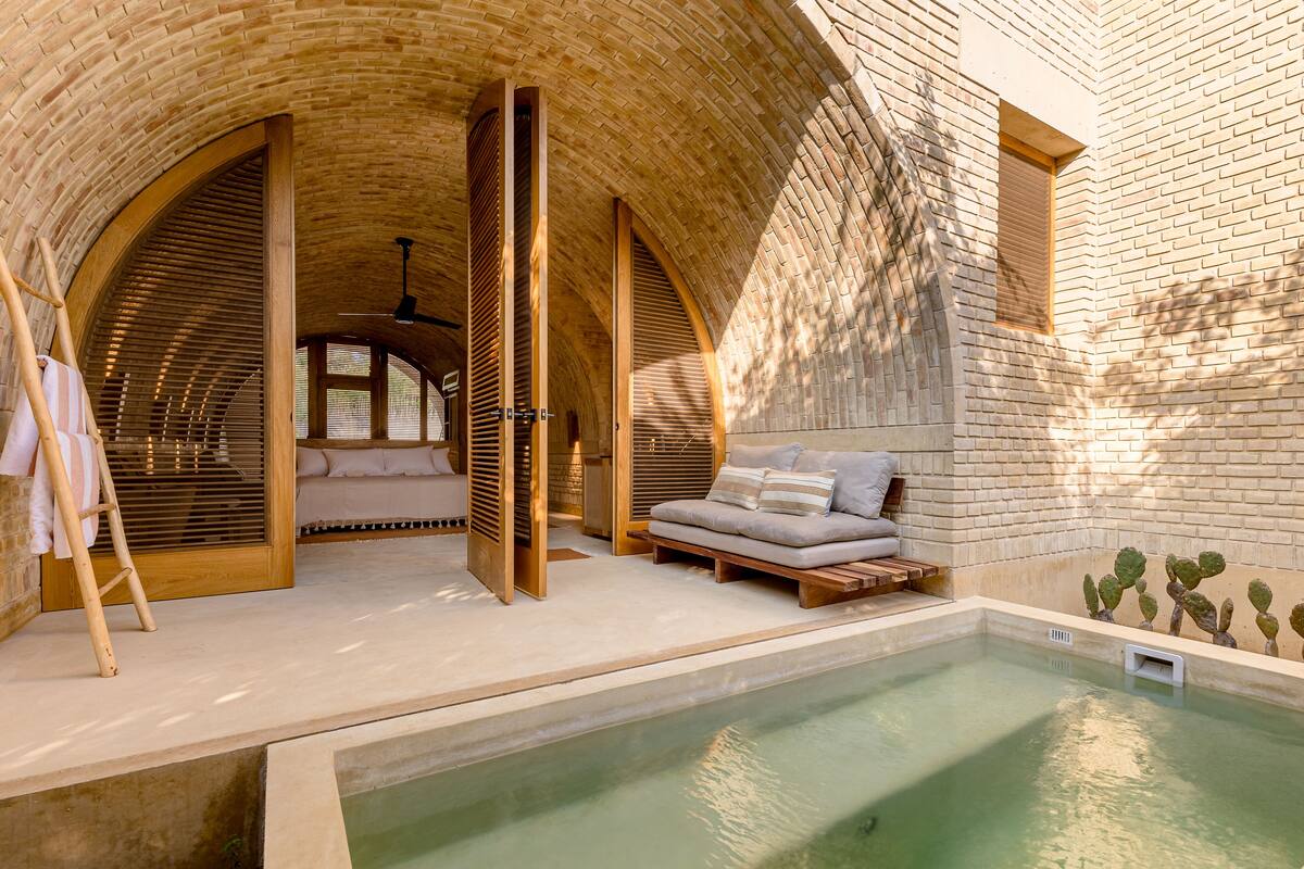 A spa area with a pool, wooden arches, and a seating area with cushions.