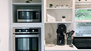 Eine Küche mit Mikrowelle, Backofen und Kaffeemaschine. Regale mit Dekoration und ein Willkommensschild.