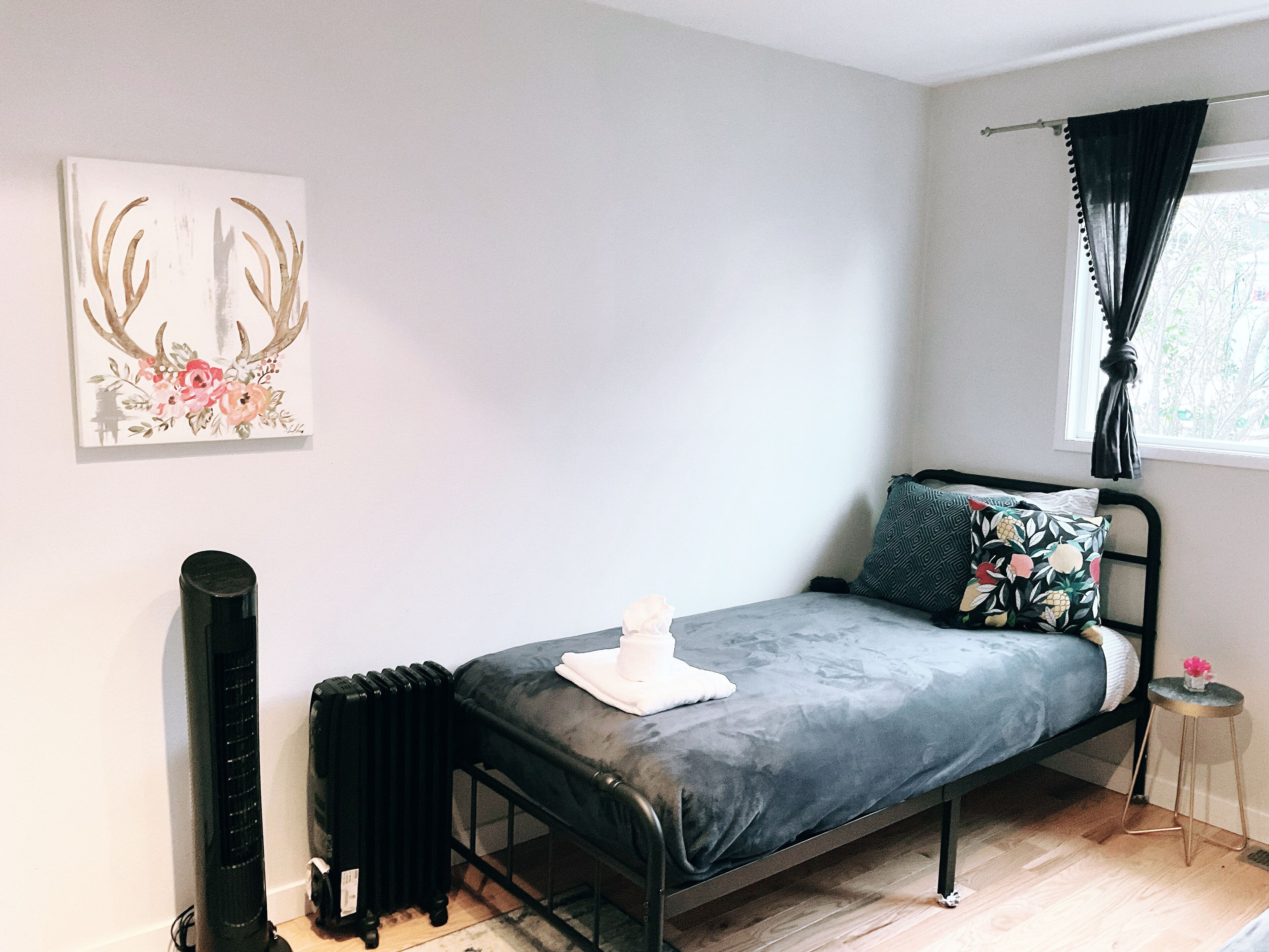 A small, modern bedroom with a single bed, a radiator, a window with curtains, and a wall-mounted artwork.