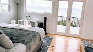 Ein Schlafzimmer mit Bett, Nachttisch mit Lampe, kleinem Schreibtisch und Balkon mit Blick.