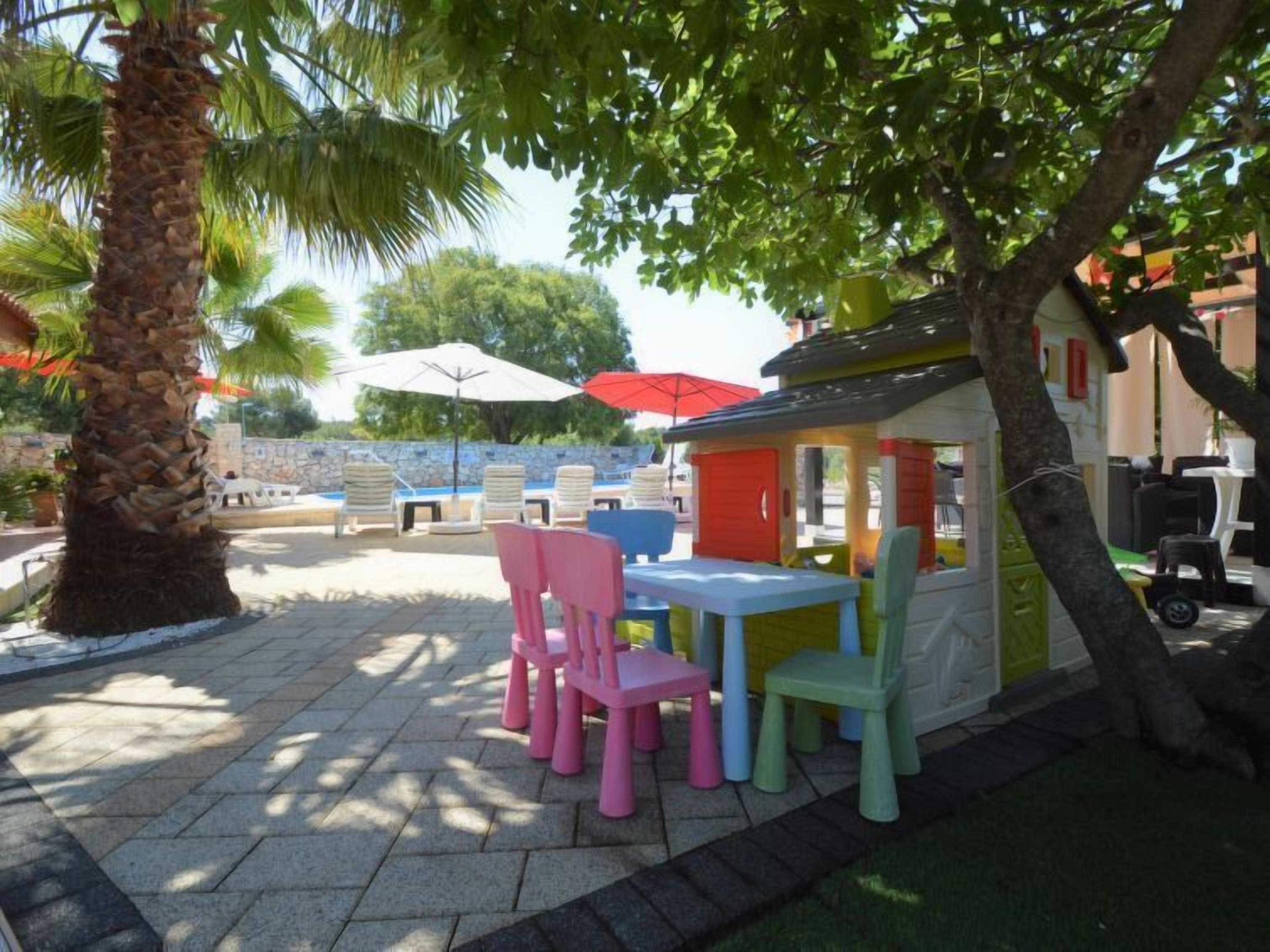 An outdoor patio area with stone flooring, colorful plastic chairs, and umbrellas.