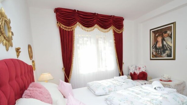 Un cuarto de hotel con un cabecero tapizado en rojo, una cama con ropa de cama floral, una mesita de noche con una lámpara y un cuadro en la pared.
