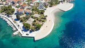 An aerial view of a coastal area with a curved beach, a marina with boats, and residential buildings.