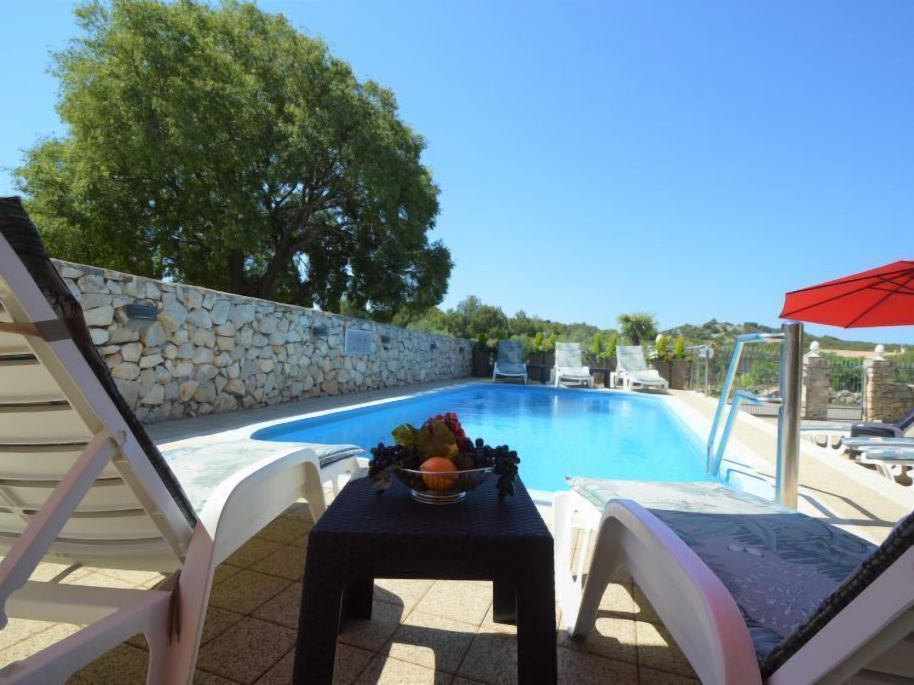A pool area with lounge chairs and a table with fruit.