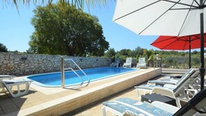 An outdoor swimming pool with lounge chairs and an umbrella.