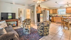 A spacious living room with a sofa, armchairs, a coffee table, and a TV. The kitchen area includes wooden cabinets, a refrigerator, and a dining table with chairs. - 2 Mi to Beach: Canal-Front Home in Hudson! (Hudson)