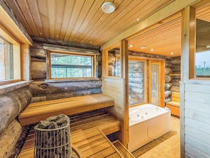 A log cabin interior with a stone bench, a bathtub, and a window overlooking a forest.