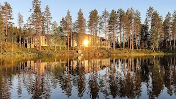Una baita circondata da alberi alti e un lago tranquillo che riflette l'edificio.