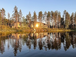 A cabin surrounded by tall trees and a calm lake reflecting the structure. - Jussis chalet a by Interhome (Kuusamo)