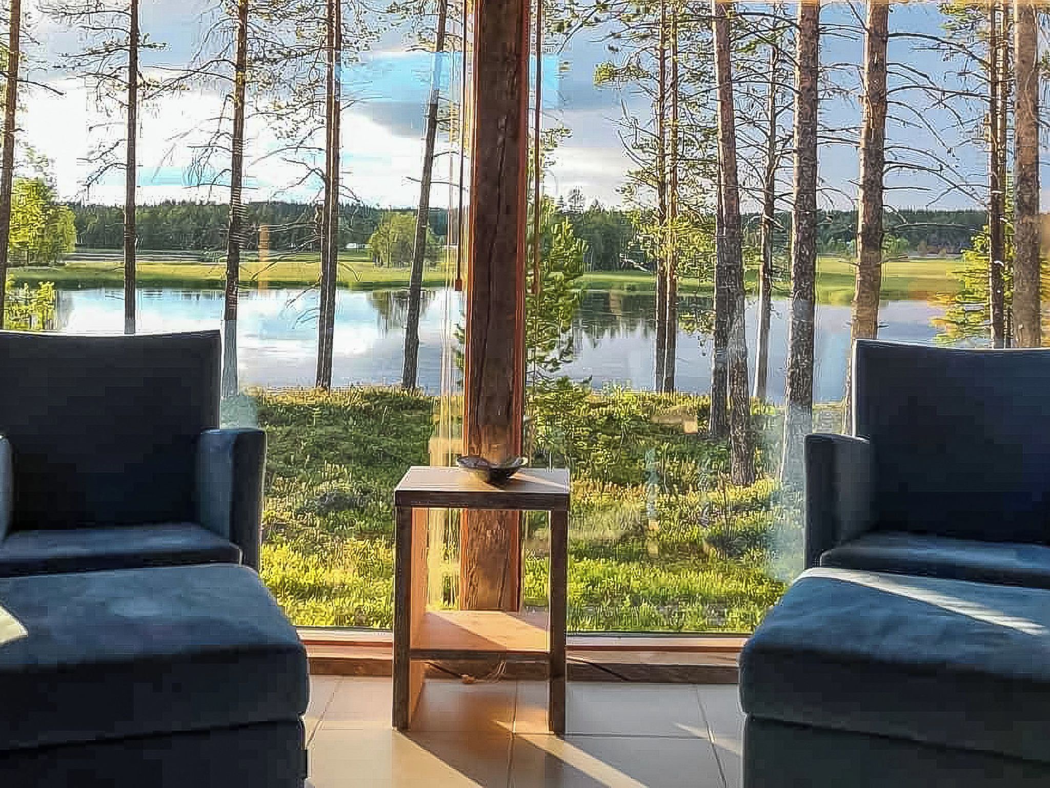 Huoneessa on kaksi tuolia, jotka on sijoitettu vastakkain suurten ikkunoiden eteen. Ikkunoista avautuu näkymä järvelle ja puille.