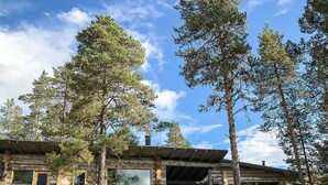 A log cabin with large windows and a covered porch, surrounded by tall pine trees. - Jussis chalet a by Interhome (Kuusamo)