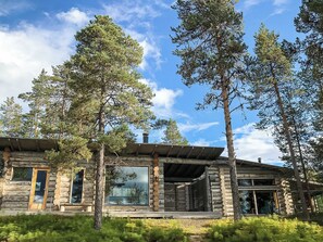 A log cabin with a large glass window, surrounded by tall pine trees.