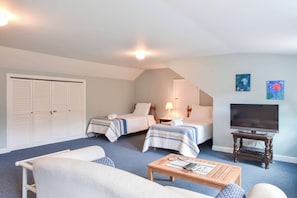 A hotel room with two beds, a sofa, a TV, and artwork on the walls.
