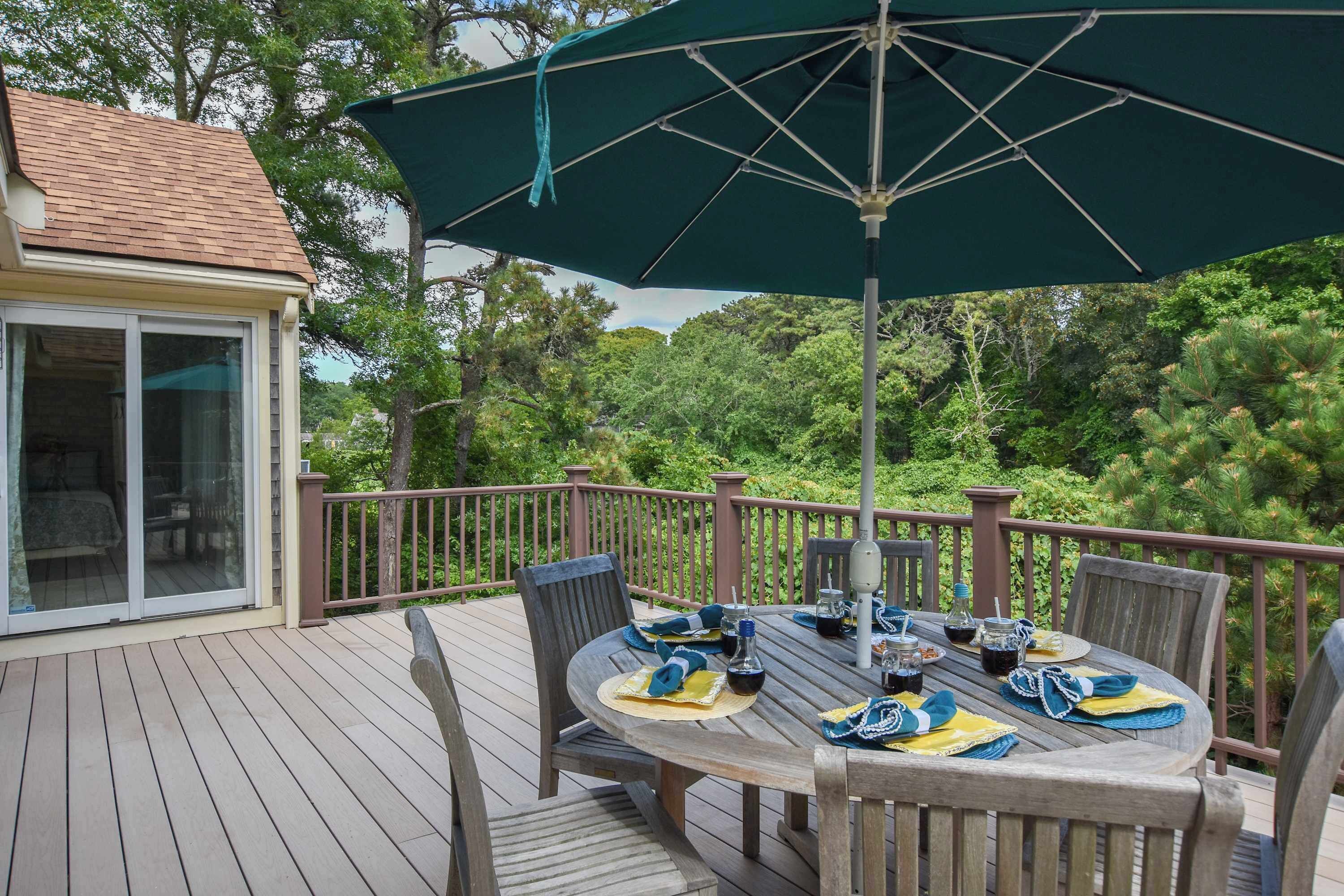A deck with a table set for dining, surrounded by chairs, and an umbrella providing shade.