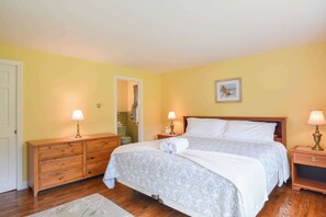A hotel room with a bed, wooden dresser, nightstands, and a bathroom visible through an open door.