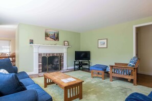 Una sala de estar con chimenea, televisor, sofá, banqueta y un cuadro en la pared.