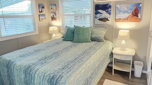 Een slaapkamer met een bed, twee nachtkastjes met lampen, een plafondventilator en een raam met jaloezieën.